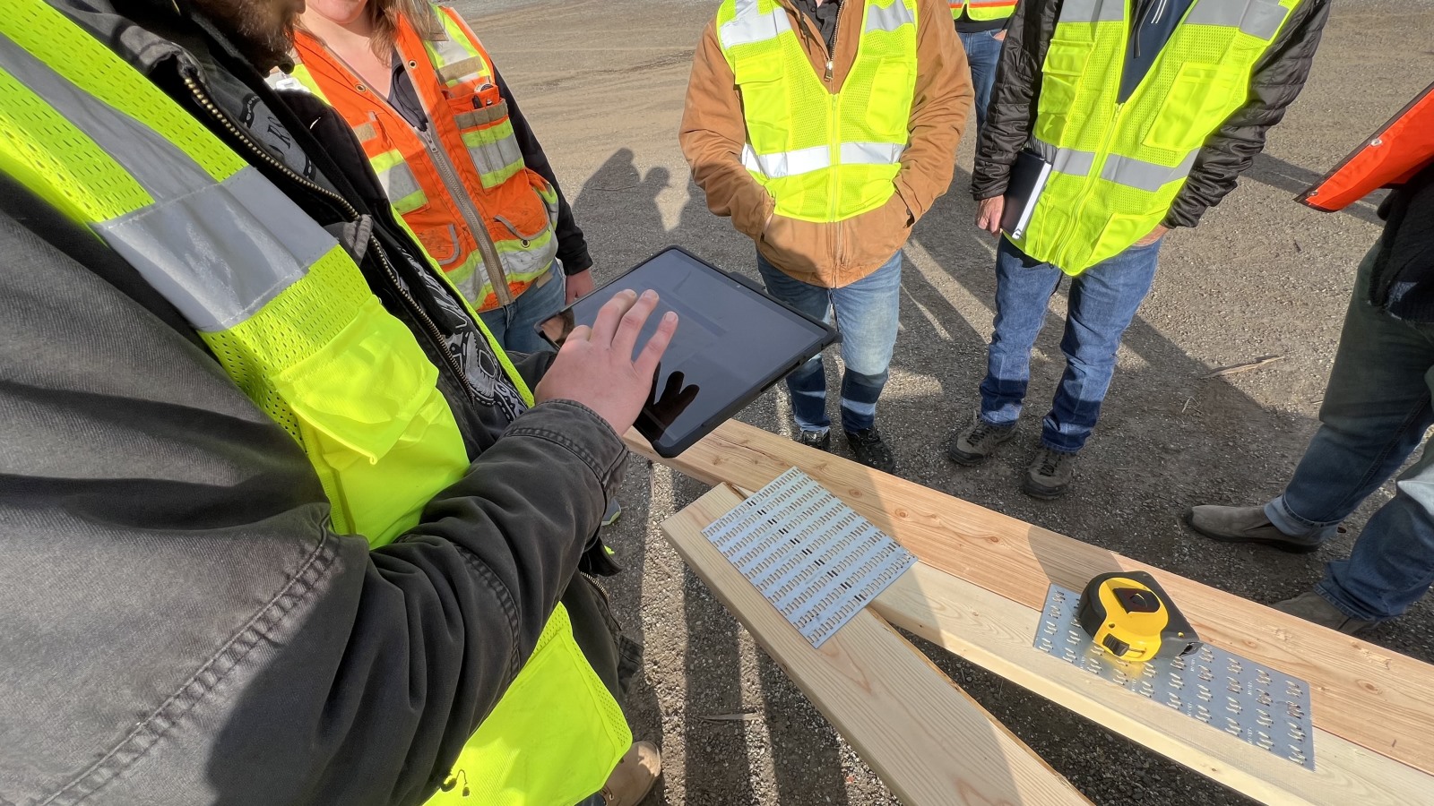Construction workers circling up around an iPad over a roof frame.