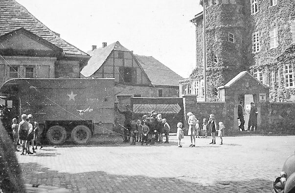 A group of children standing in front of a military truckDescription automatically generated