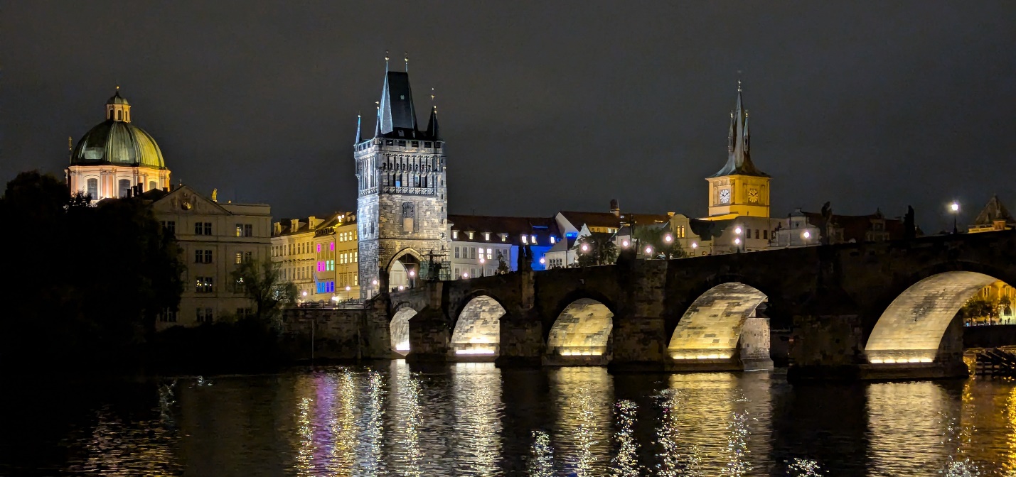 A bridge over water with buildings and lights at nightDescription automatically generated