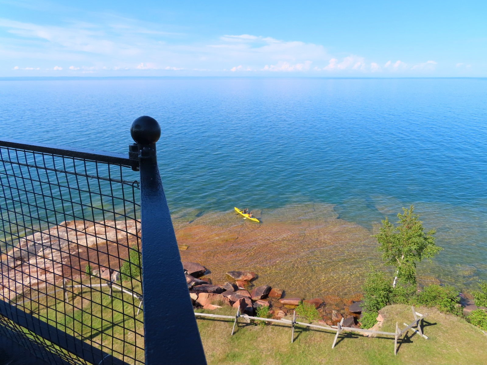 Photo of a view from the top of Sand Island Lighthouse with rocks, a colorful water bottom, and a kayak